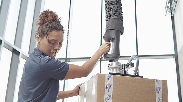 Woman transports cartons with tube lifter Force-Lift in a production hall