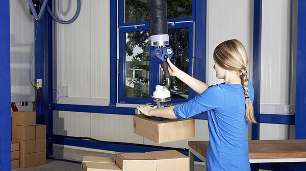 Woman operates tube lifter FLEX-LIFT to lift a box