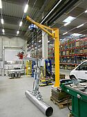 Crane and rail system with vacuum lifter lifting a pipe in a production hall
