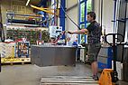 Man transporting metal box with the help of off-grid battery operated vacuum lifter in workshop