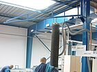 Man operates tube lifters attached to a crane and rail system in a production hall