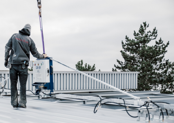 Zimmermann auf dem Dach beim Heben mit dem Vakuumhebegerät CLAD-BOY von Dachpaneelen