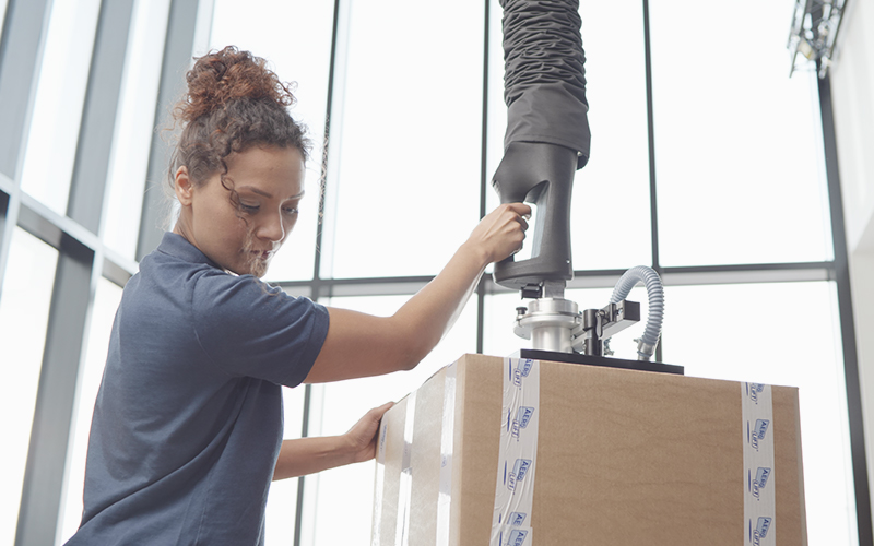 Woman transports cartons with tube lifter Force-Lift in a production hall